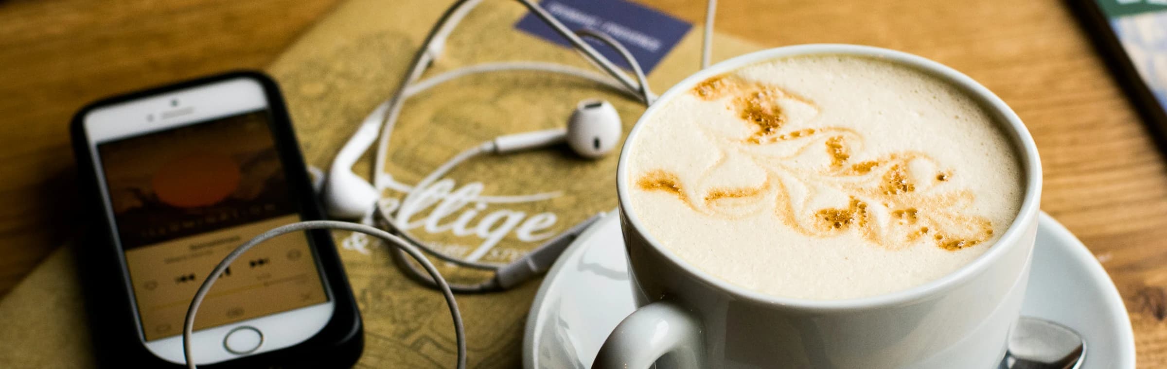 A phone and earphones beside a cup of coffee